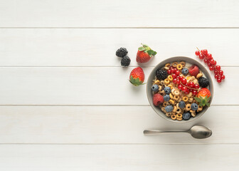 Cereal bowl with berries and spoon on a white table, top view, copy space