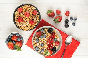 Cereal bowls with berries on a red napkin on a white table, top view