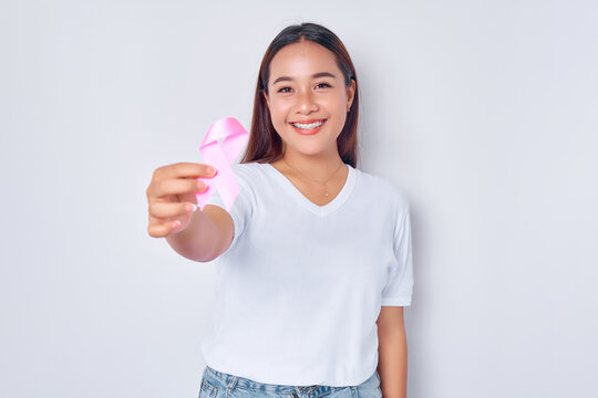 smiling young blonde woman girl Asian wearing casual white t-shirt holding in hand pink silk ribbon isolated on white background. Breast Cancer Awareness concept