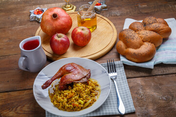 Spelled with vegetables and duck leg in a plate next to challah, wine, honey and apples with pomegranate for the Rosh Hashanah meal.