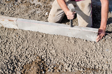Builder placing edging pin kerb on semi-dry concrete using a string line to keep them straight during construction of the footpath