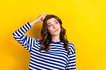 Photo of attractive young woman scratch head look interested empty space dressed stylish striped outfit isolated on yellow color background