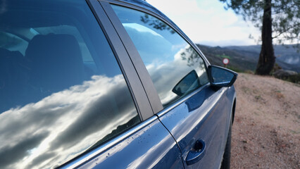 Naklejka premium Coche aparcado en la naturaleza con el reflejo de las nubes en el cristal
