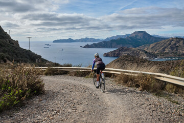 female cyclist riding a gravel bike on a gravel road with a view of the mountains, Alicante region of Spain