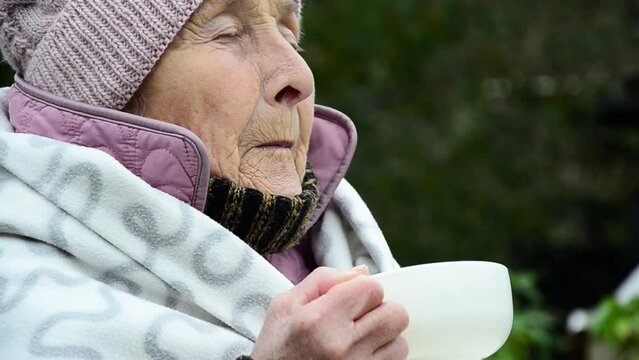 Winter in Ukraine during the war. War in Ukraine. Peaceful Ukrainian population. Russian aggression against Ukraine. The old grandmother is getting warm. The face of an elderly woman. wrinkles