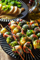 Skewers with fresh Brussels sprouts wrapped with bacon on table - dark and moody