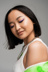 portrait of brunette asian woman with makeup and purple eyeliner isolated on grey.