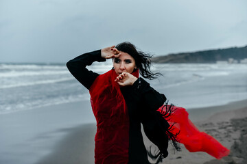 Portrait woman in black dress walking with red scarf on the winter beach