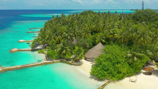 Tropical beach villas with thatched roofs and coconut trees with turquoise sea. Aerial drone view.