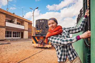 Young woman posing at old wagon or diesel locomotive at empty abandoned Wadi Rum train station