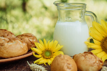 mug of homemade farm fresh milk and pies or buns, sunflower, baked goods on a wooden background