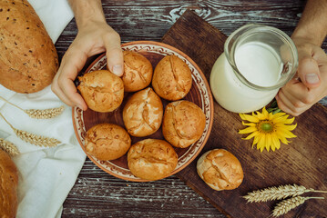 man holding pies or buns in his hand and a mug of homemade farm fresh milk, baked goods and bread with flax seeds on a wooden table 1