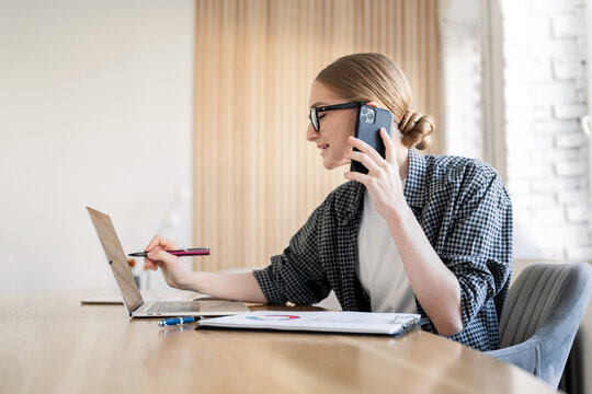 A Perfectionist Is A Business Woman In Glasses And A Shirt, Talking On The Phone And Using A Laptop In The Office, Checking A Report Online.