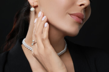 Young woman with elegant pearl jewelry on black background, closeup