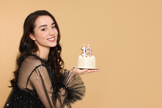 Coming of age party - 18th birthday. Smiling woman holding delicious cake with number shaped candles on beige background, space for text
