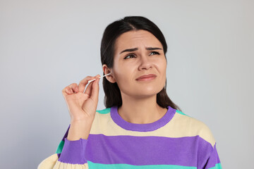 Young woman cleaning ear with cotton swab on light grey background