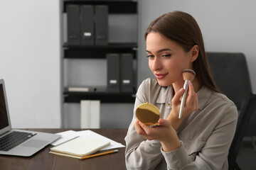 Young woman with cosmetic pocket mirror doing makeup at table indoors, space for text