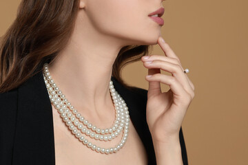Young woman wearing elegant pearl jewelry on brown background, closeup