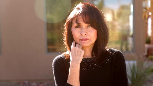 Attractive woman looking at camera with arm to face outside back lit