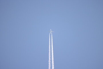 The plane flies in the distance with smoke from burning fuel on a blue background without clouds