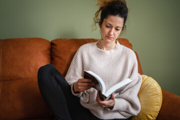 One woman caucasian female sit on the sofa bed at home read book