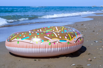 an inflatable ring in the shape of a donut lies on the sand against the background of the blue sea