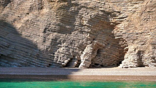 Rock geology layers visible at cliffs near Chomi or Paradise beach at Liapades, Greece, calm green sea in foreground. View from a boat