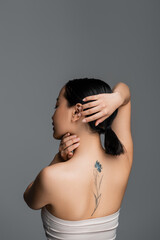 Obraz premium Side view of tattooed asian woman touching hair isolated on grey.