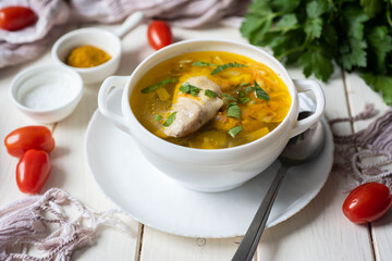 A hearty lunch dish for the whole family: chicken soup with vegetables in a white plate on a white background. Delicious chicken broth. Close-up