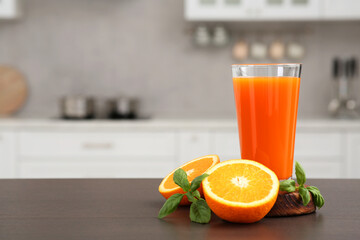 Glass of tasty orange juice and fruit on wooden counter in kitchen, space for text