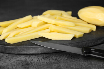 Whole and cut raw potatoes with knife on grey table, closeup. Cooking delicious French fries