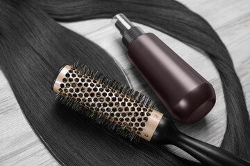 Spray bottle with thermal protection, lock of brunette hair and hairbrush on white wooden table, closeup