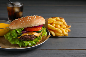 Delicious burger, soda drink and french fries served on grey wooden table. Space for text