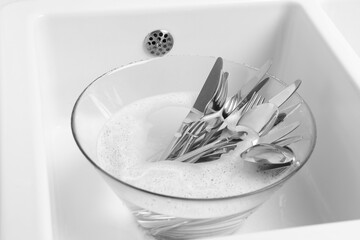 Washing silver spoons, forks and knives in kitchen sink