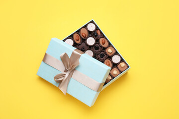 Open box of delicious chocolate candies on yellow background, flat lay