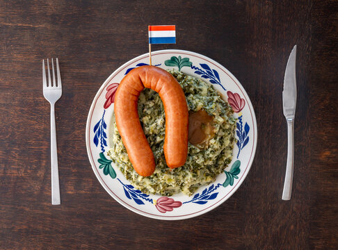 A plate with 'Stamppot Boerenkool met worst' traditional dutch meal consisting of potatoes mashed with kale, smoked sausage and gravy
