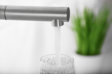 Filling glass with tap water from faucet on blurred background, closeup