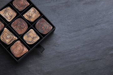Box of tasty chocolate candies on black table, top view. Space for text