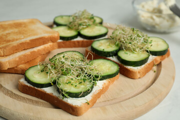Tasty toasts with cucumber, cream cheese and microgreens on white table, closeup