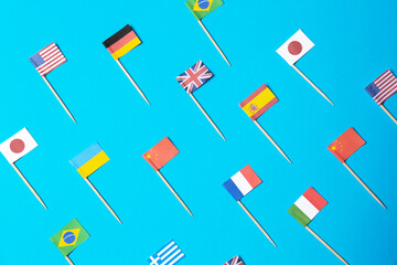 Many small paper flags of different countries on light blue background, flat lay