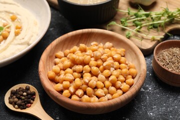 Delicious chickpeas and different products on black textured table, closeup. Hummus ingredient