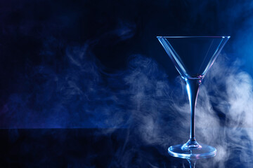 Empty clean martini glass on mirror table against black background, space for text