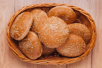 Wicker basket of fresh buns with sesame seeds on wooden table, top view