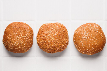 Fresh buns with sesame seeds on white tiled table, flat lay