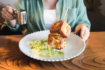 Trendy breakfast in hipster restaurant, cafe. Creative square-shaped croissant in form of cube on skewer. Served with hot cheese in small gravy boat, sauceboat. Citylife meal, meating with friend