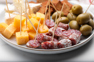 Toothpick appetizers. Pieces of sausage and cheese on white table, closeup