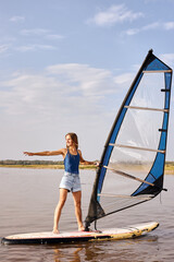 Young Female windsurfer at lake. Beautiful landscape. Summer water sports activities, recreation...
