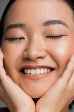 close up portrait of smiling asian woman with natural makeup touching face while smiling with closed eyes.