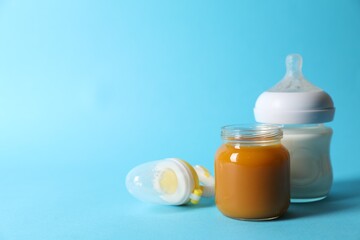 Jar with healthy baby food, bottle of milk and fruit feeder on light blue background. Space for text