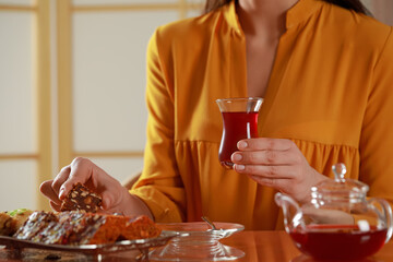 Woman with glass of traditional Turkish tea taking sweets at table indoors, closeup